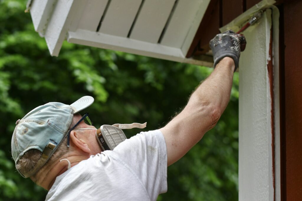 A man painting house exterior with white color